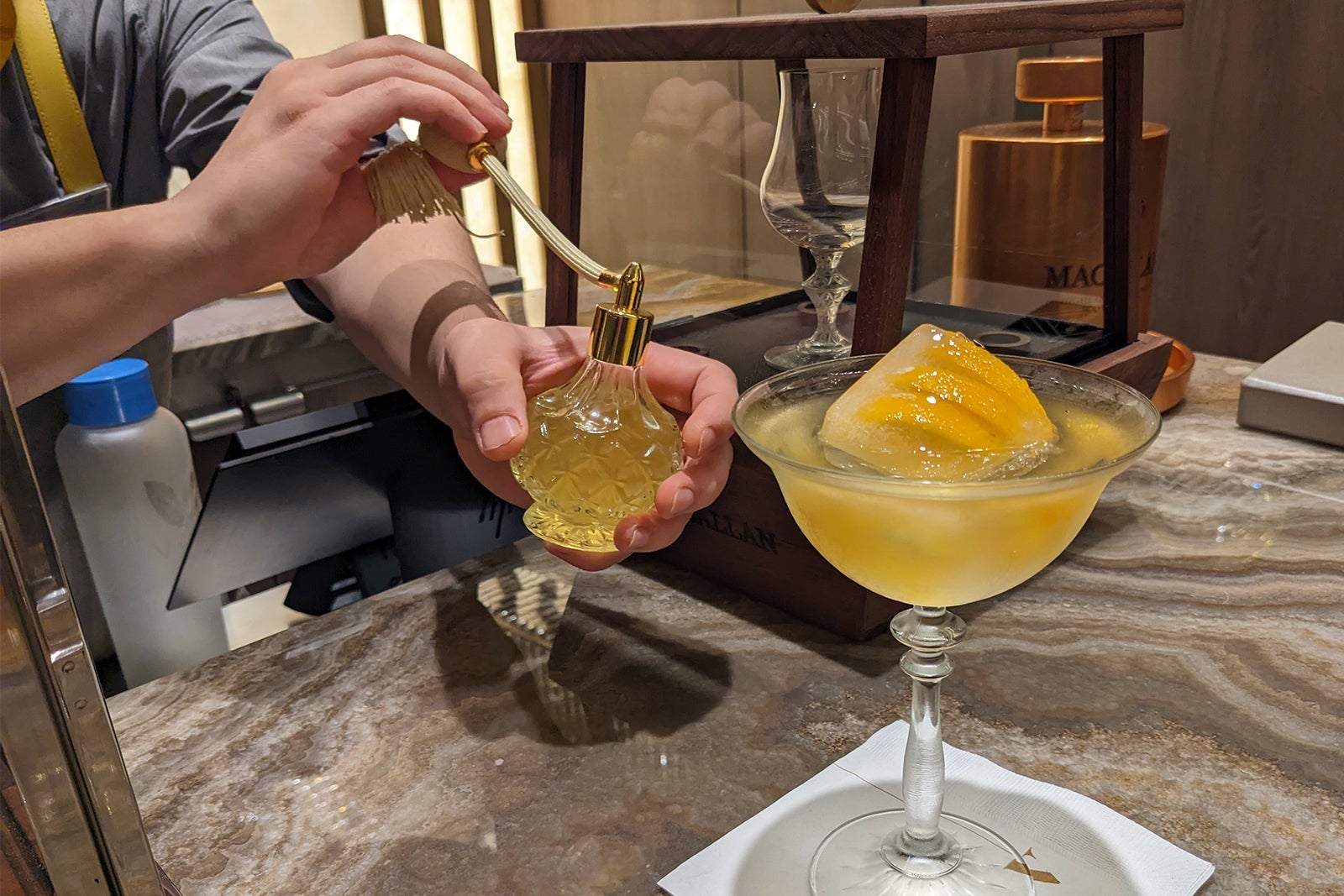 Bartender spraying orange cocktail with scent in perfume bottle