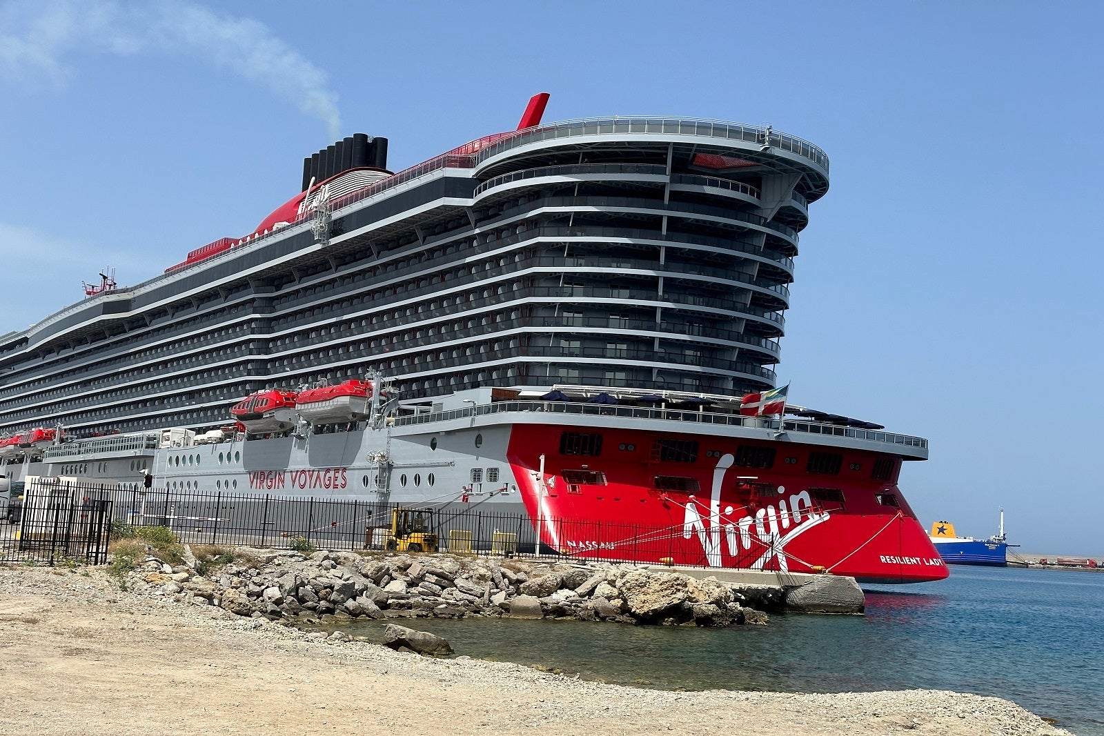 A gray cruise ship docked with a red aft that says "Virgin" in white letters
