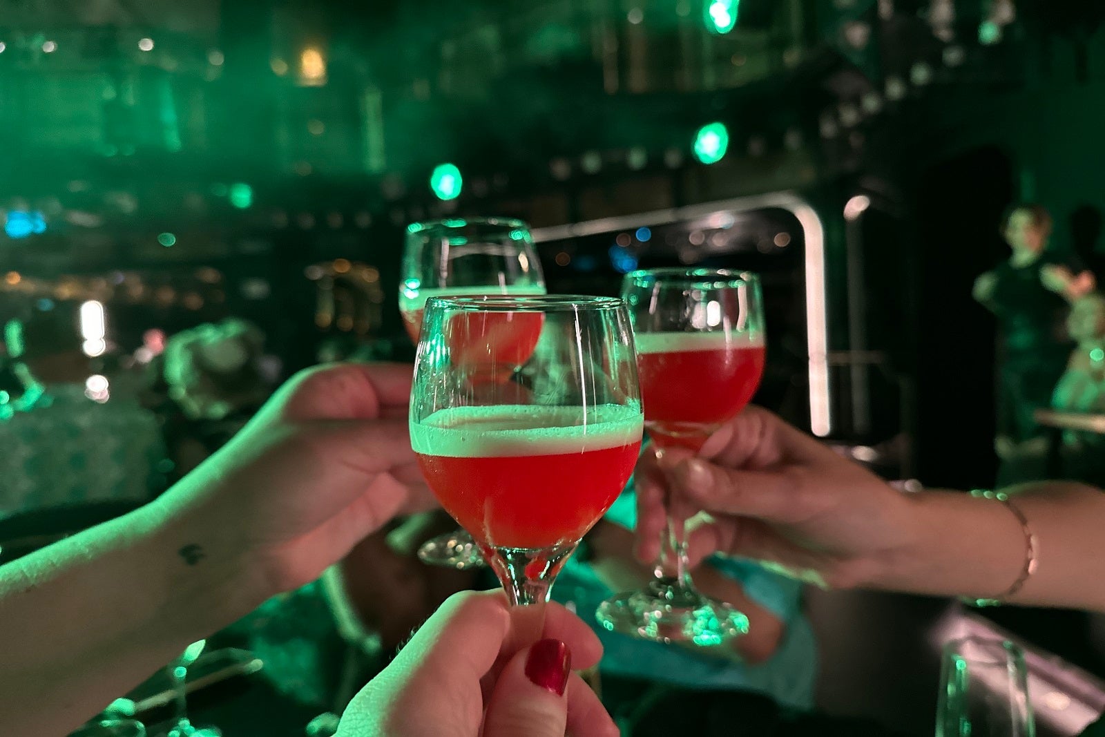 Three hands toasting glasses with red drinks in dark club