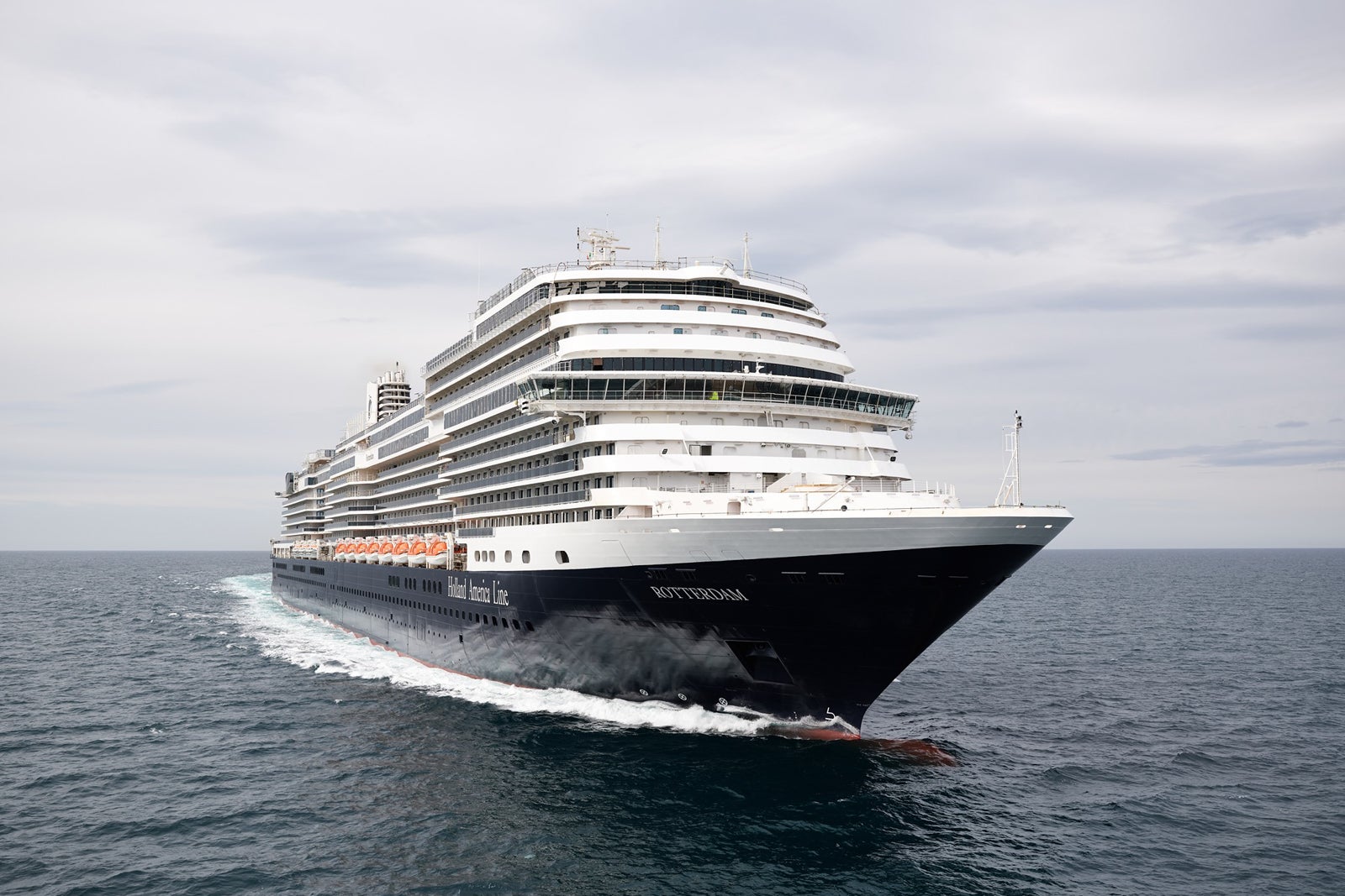 A Holland America ship sailing, creating white waves on blue water