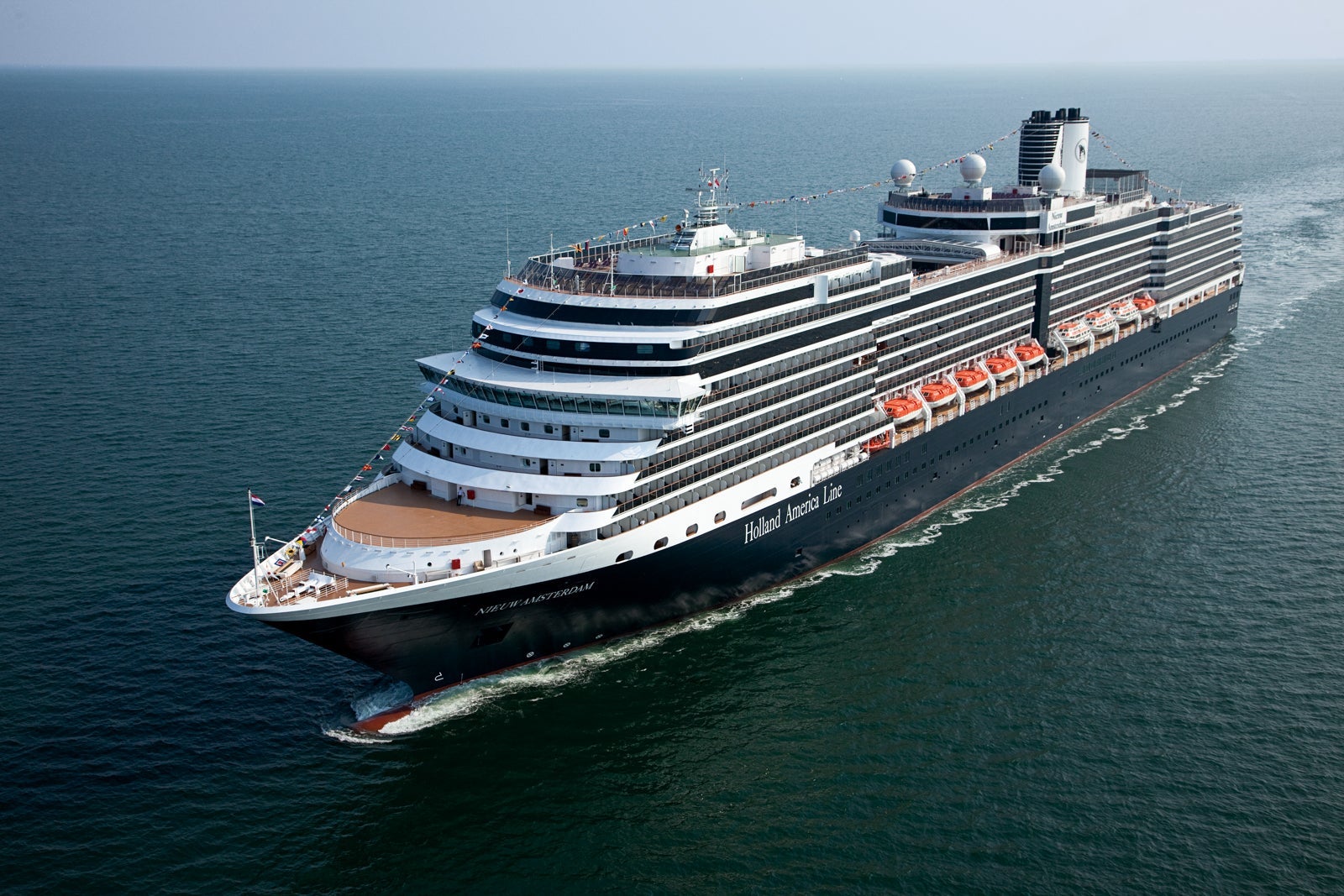 A Holland America ship sailing, creating white waves on blue water