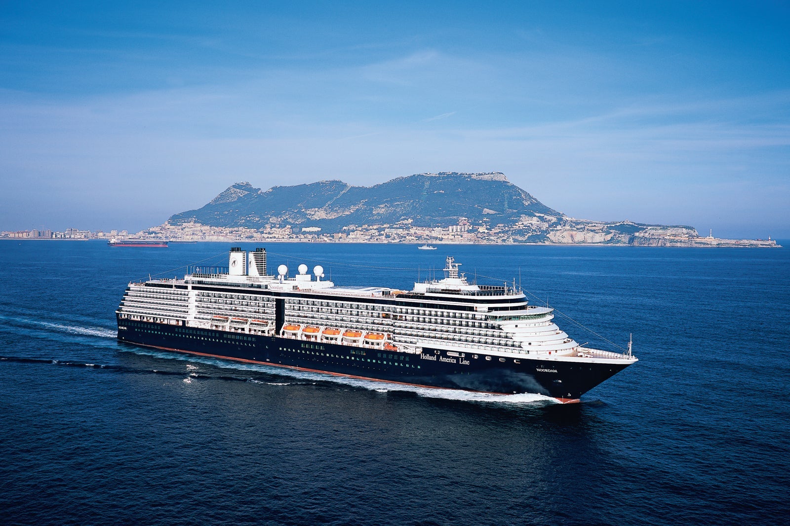 A Holland America cruise ship sails on blue water in front of a small island