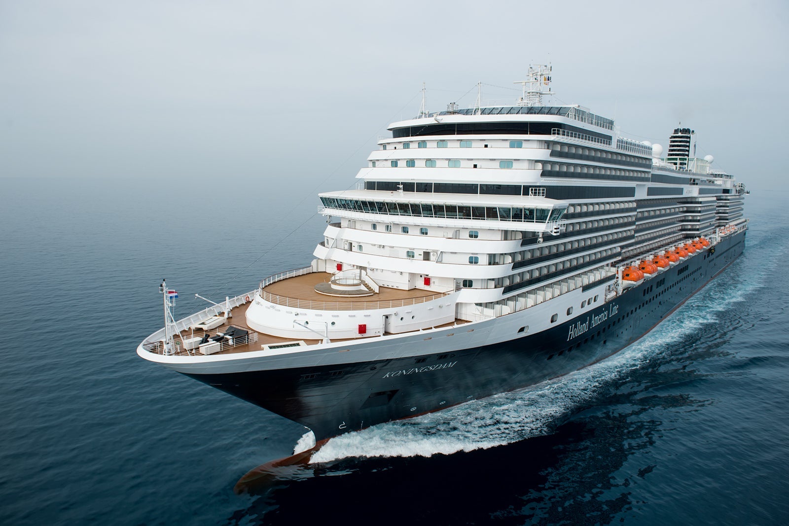 A cruise ship in motion, creating white waves on blue water