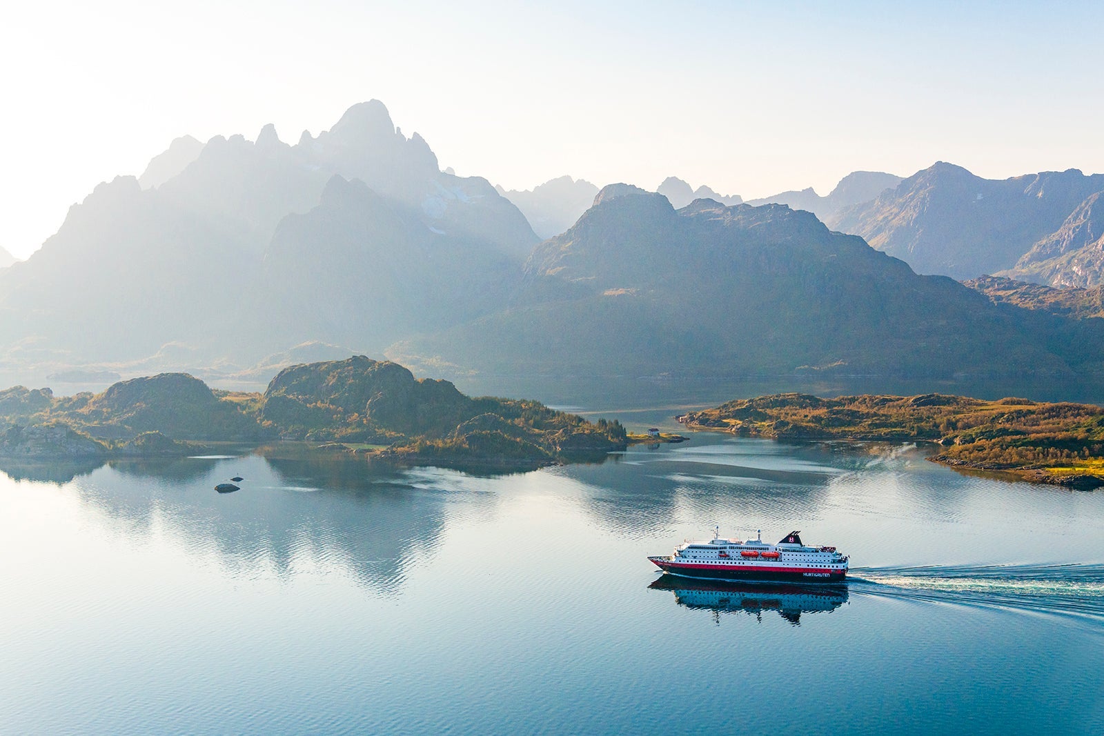 A cruise ship sailing along the coast of Norway with misty moutains in the background