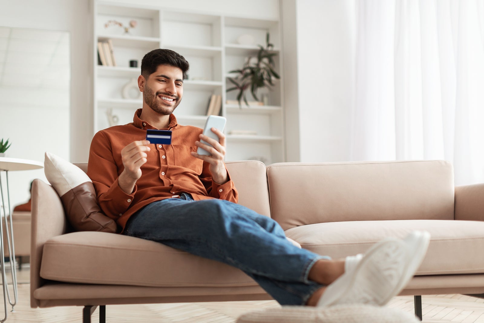 Smiling guy using phone and credit card at home
