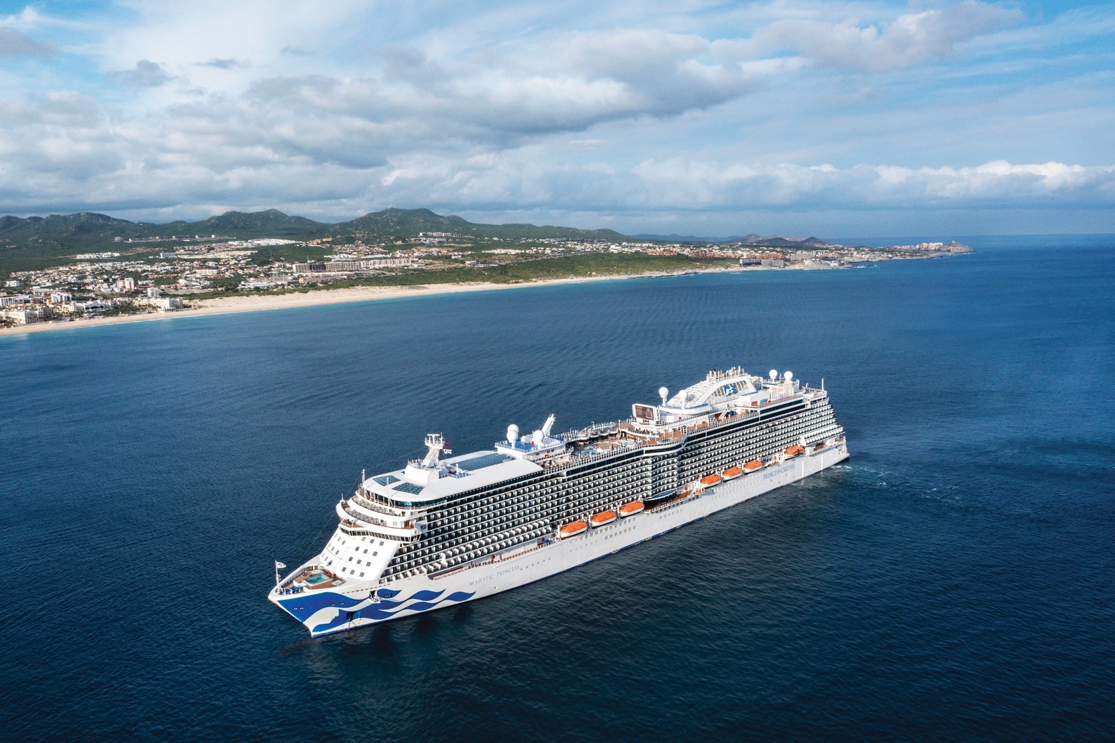 A Princess cruise ship anchored off the coast of Cabo San Lucas, Mexico, surrounded by blue water and shoreline