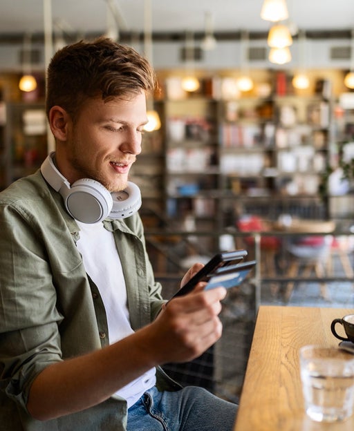 Happy man sitting and drinking coffee at cafe using his phone with credit card