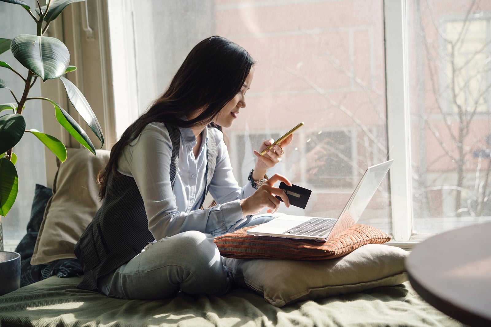 Woman using her phone and laptop with a credit card