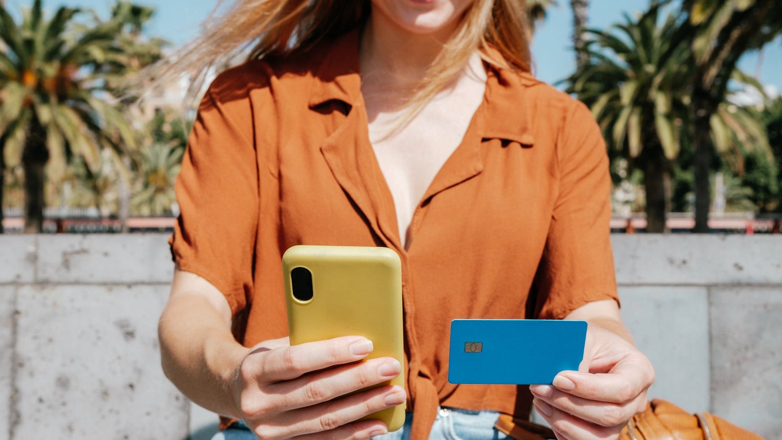 unrecognizable young woman buying online in a park with her phone and credit card