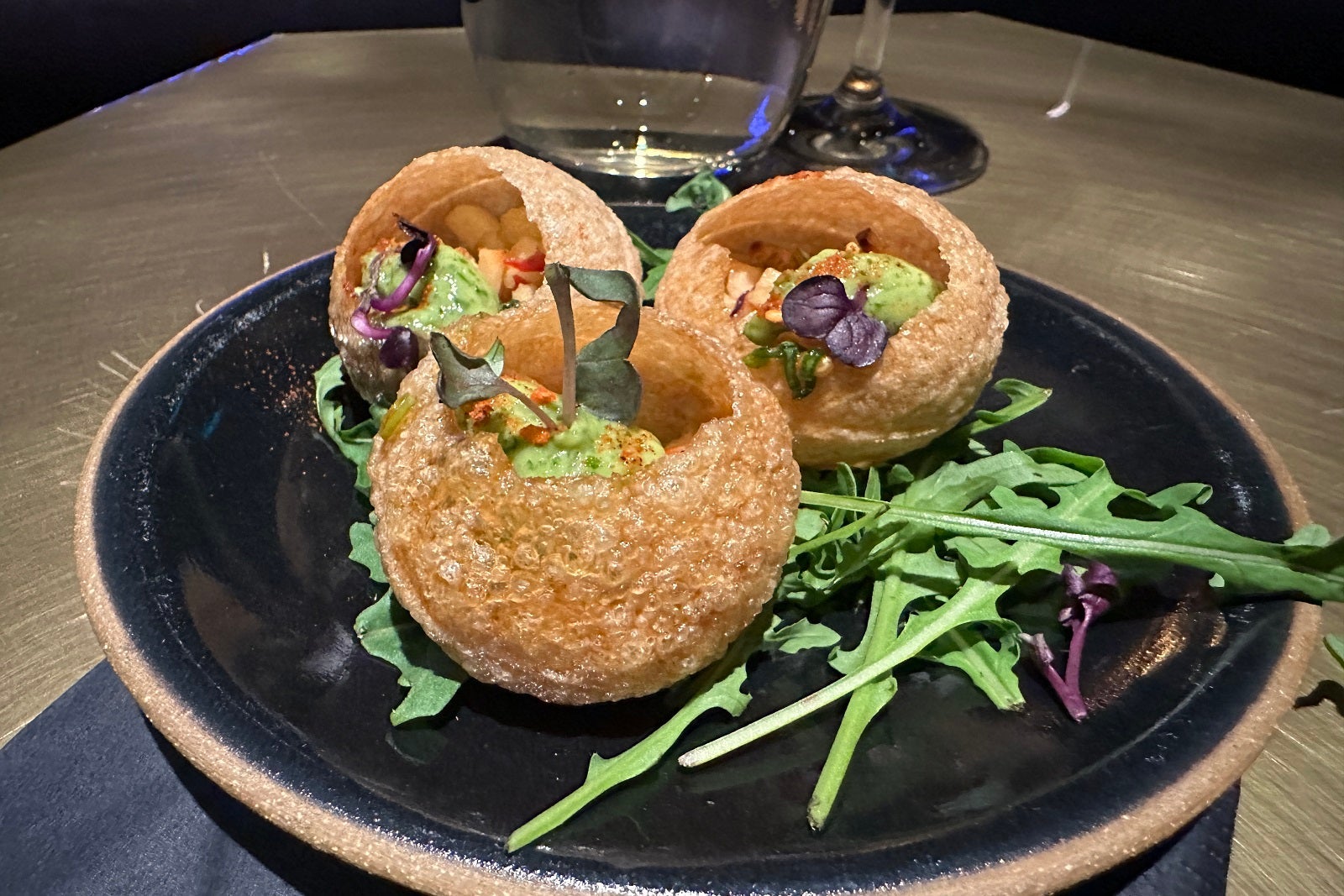 Three puff pastries filled with avocado and greens on a small, round stone plate