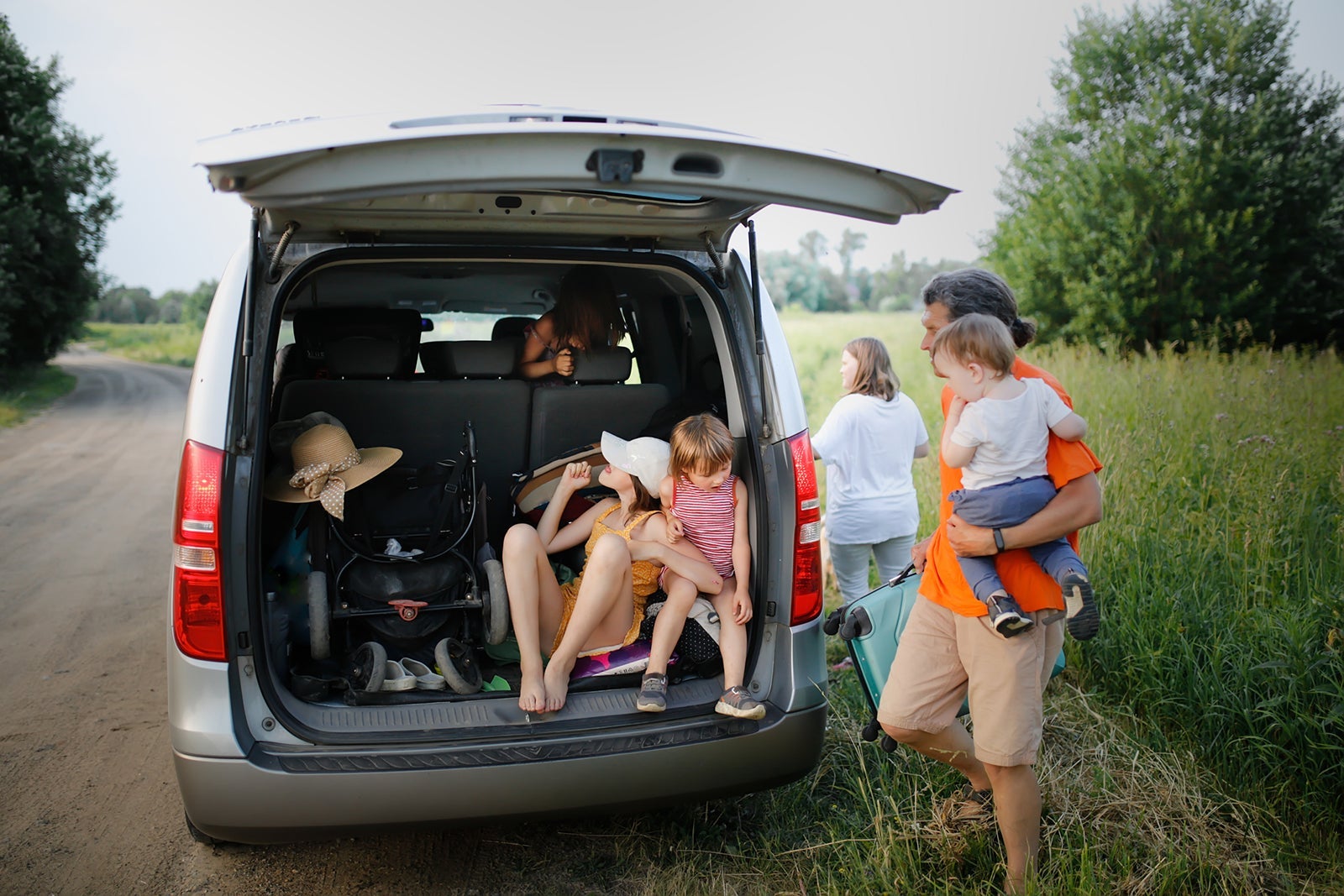 Crazy funny kids sisters play in trunk large car in summer trip, Dad and child loading suitcase into car