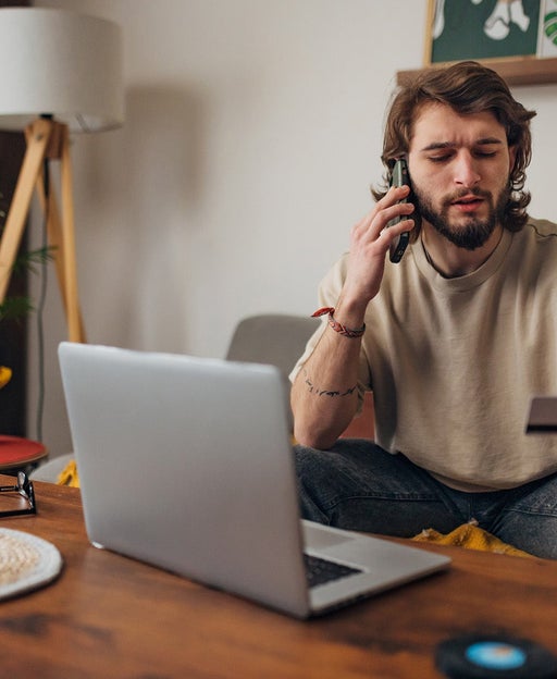 Man makes a phone call while trying to make an online purchase using a credit card and a laptop
