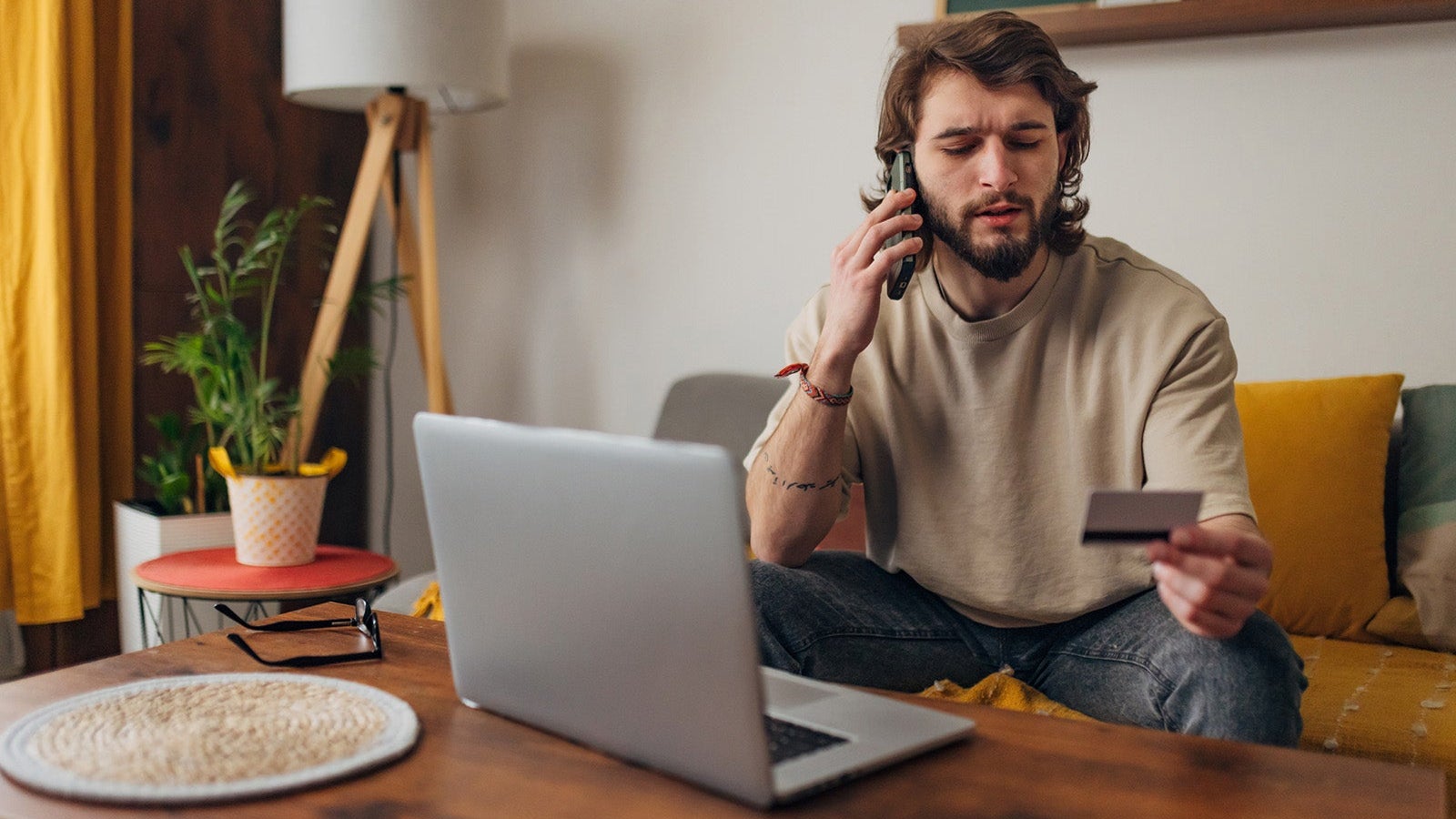 Man makes a phone call while trying to make an online purchase using a credit card and a laptop