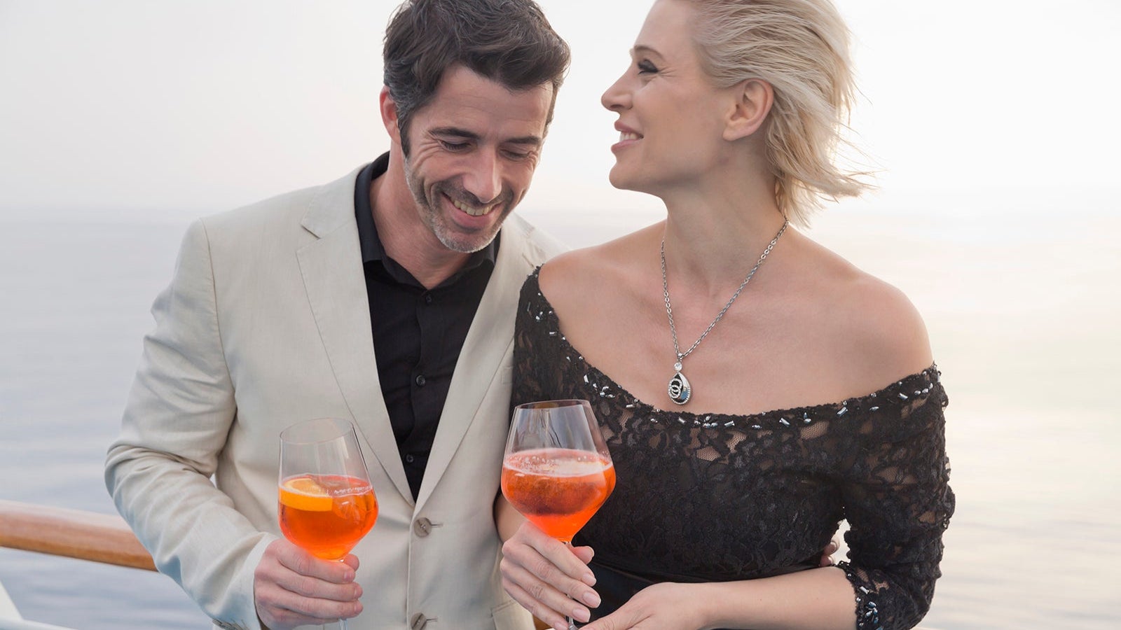 Happy couple with aperitive standing on deck of a cruise liner