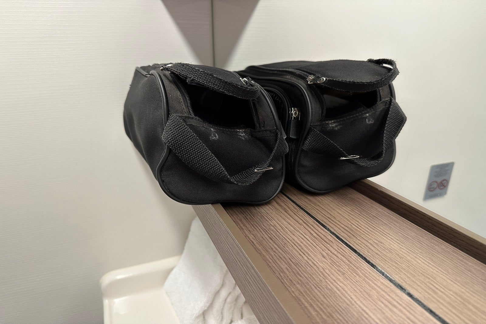 A black toiletry bag sitting on a narrow shelf in the bathroom of a cruise ship bathroom