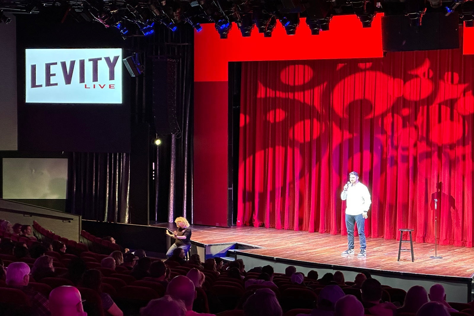 A performer on a stage in front of a red curtain in a cruise ship theater