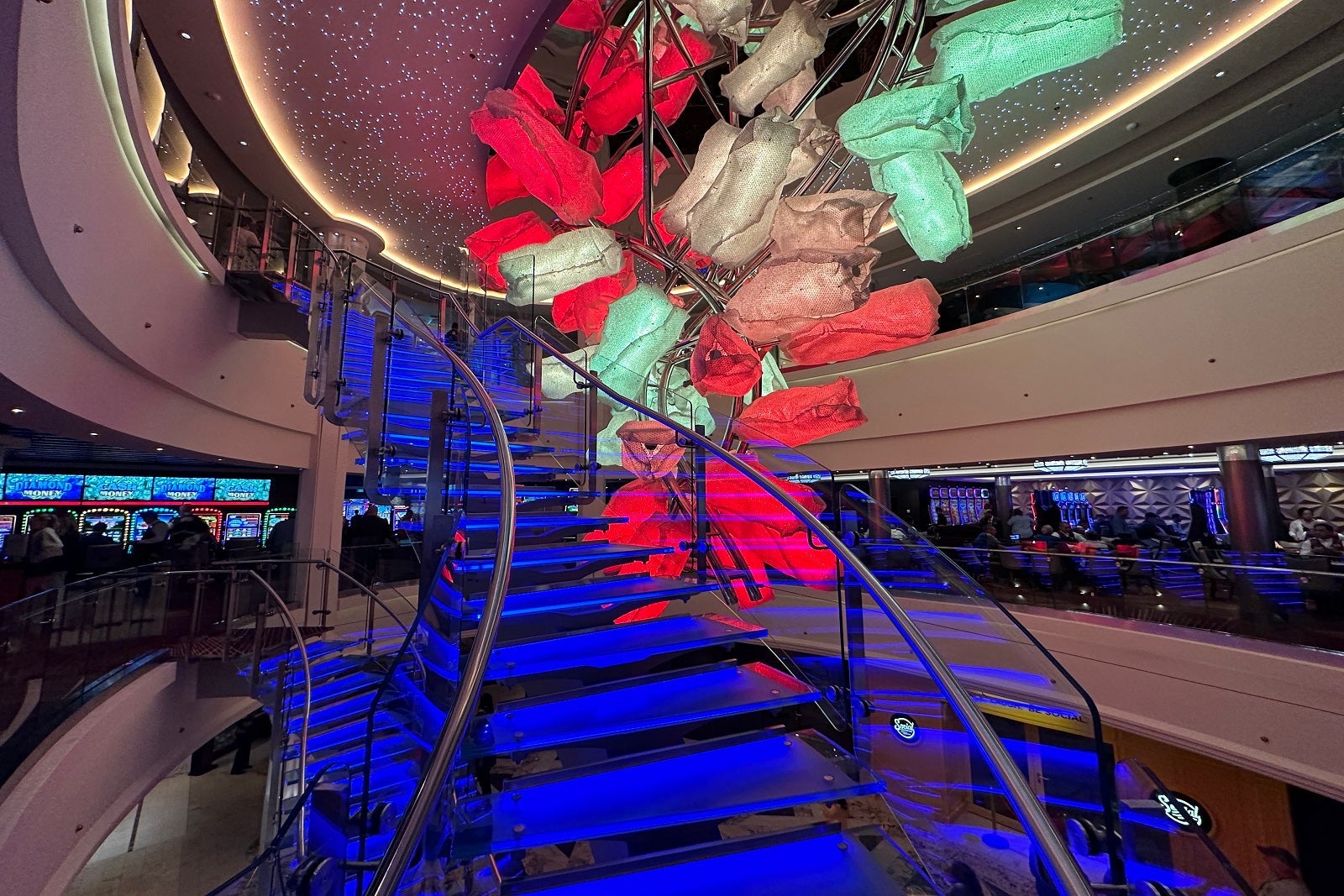 A blue winding staircase on a cruise ship with colorful red and green lights above it