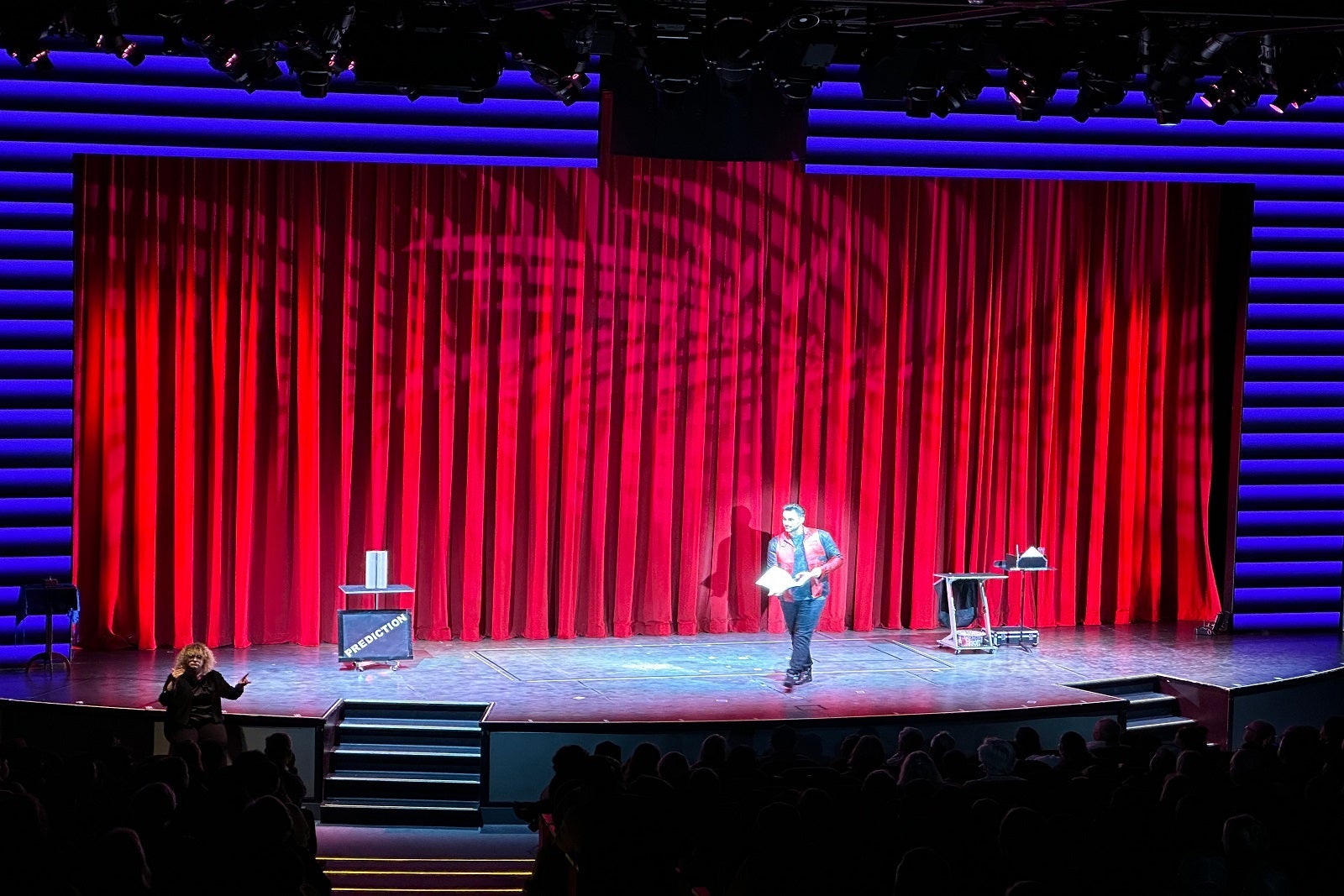 A cruise ship performer on stage in the theater in front of a red curtain