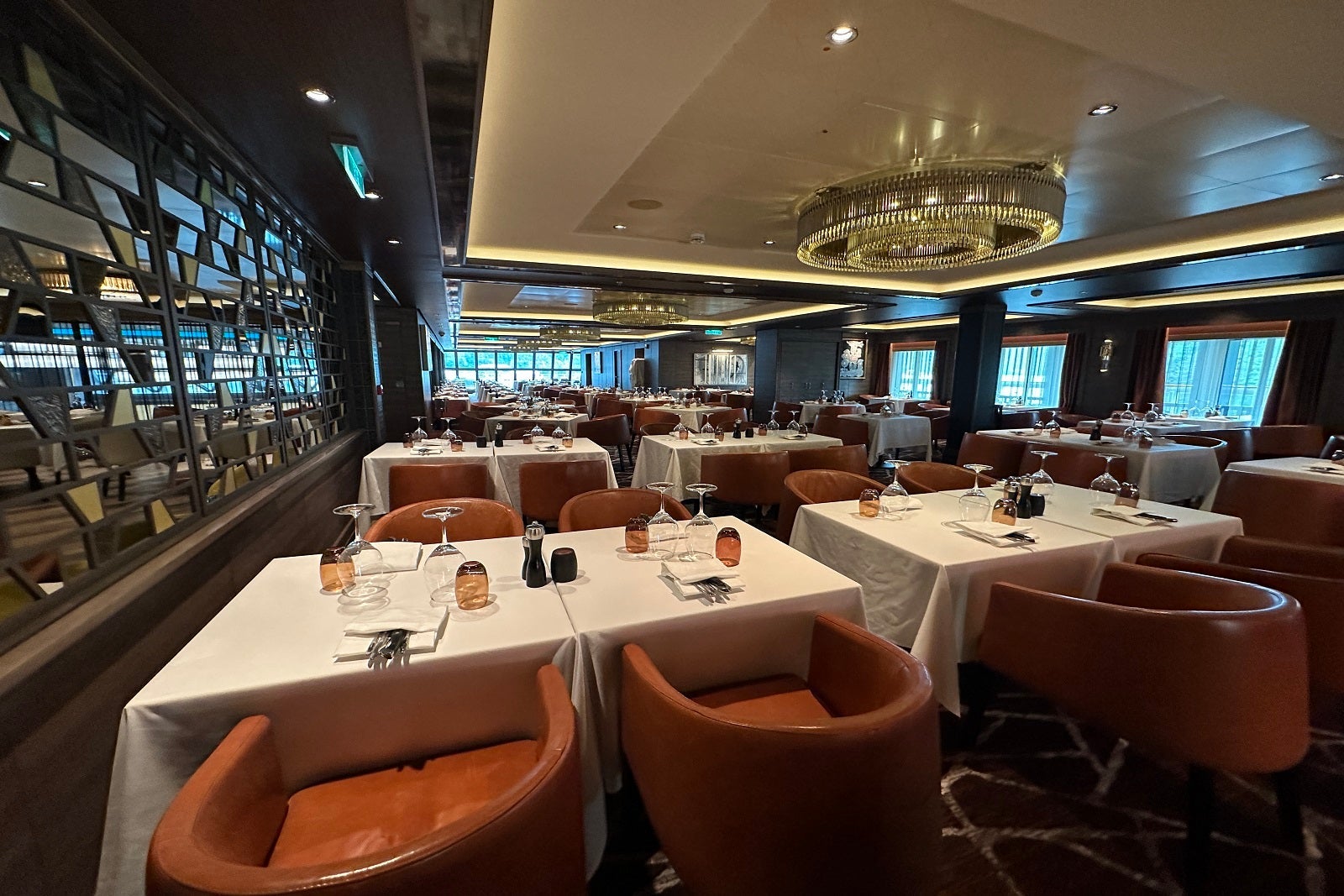 A cruise ship steakhouse restaurant with orange chairs and tables draped with white tablecloths