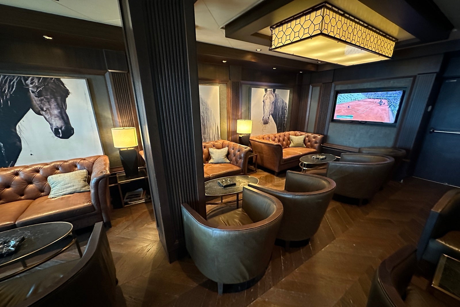A cigar lounge with dark furnishings, including tables and leather chairs and horse pictures on the walls