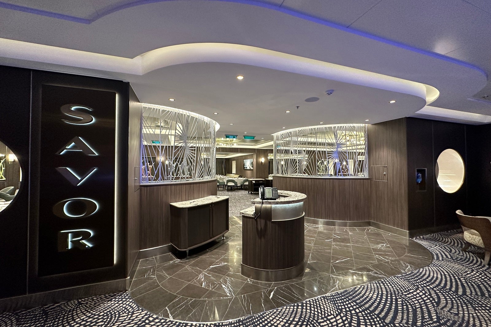 The entrance to a cruise ship main dining room with a sign on the wall that says "Savor"