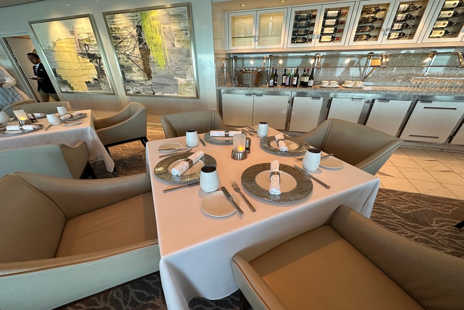 A fancy cruise ship restaurant with chairs and tables set with dinnerware and white tablecloths