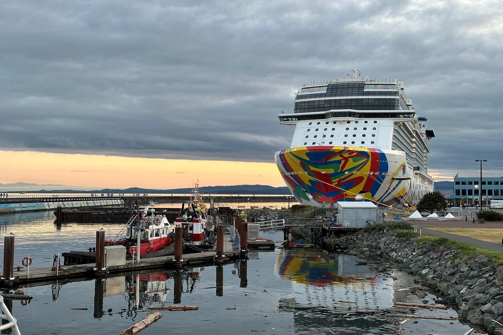 A white cruise ship with a colorful hull docked near a rocky shoreline