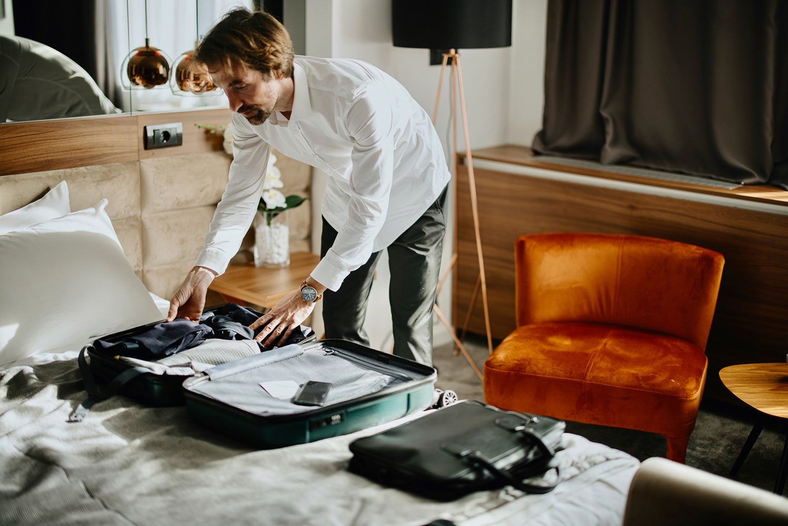 Business traveler standing above bed in the hotel room packing his Suitcase for a Trip