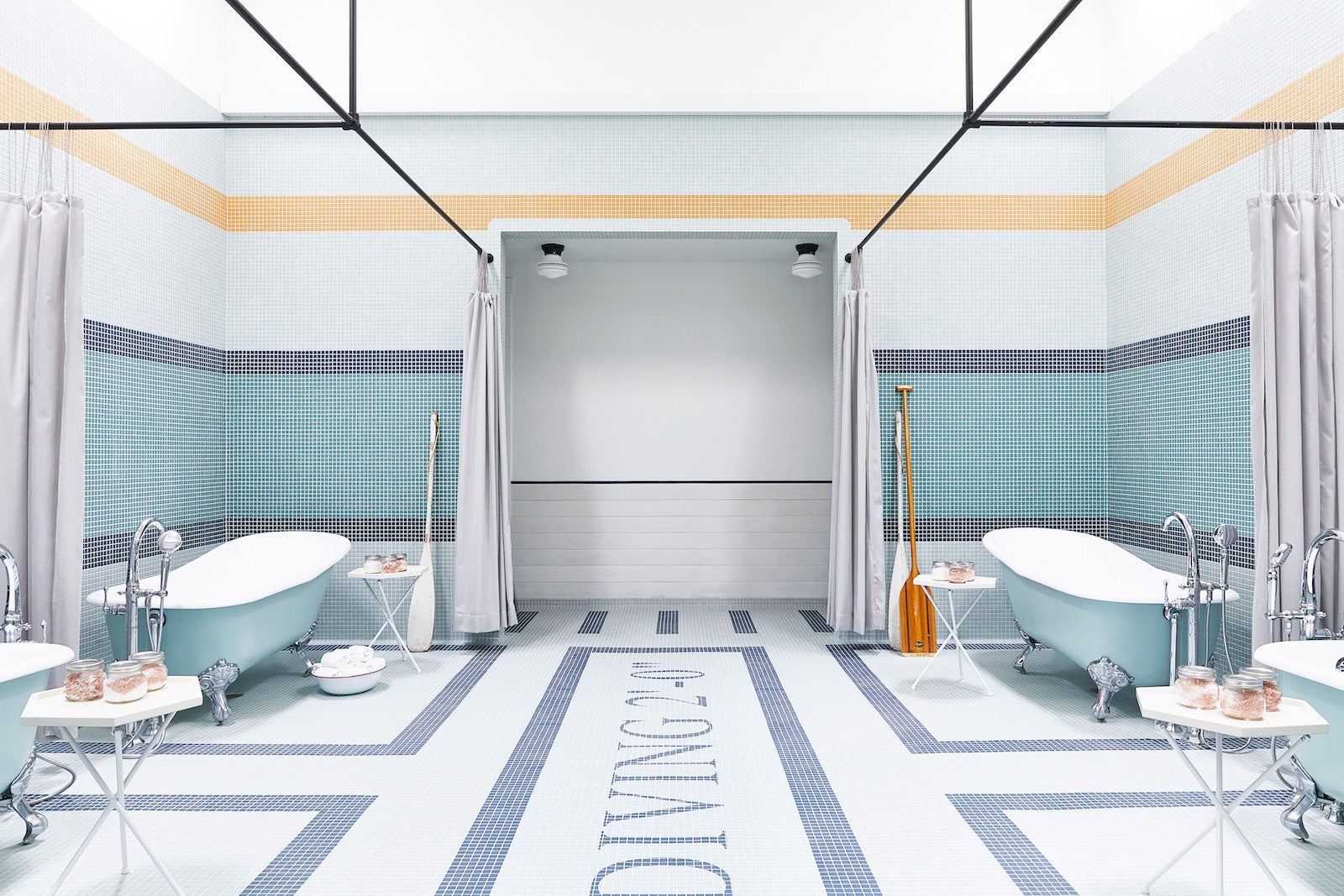 light blue, dark blue, white and yellow tiles on floor and wall with two claw-foot bathtubs on both sides of the room