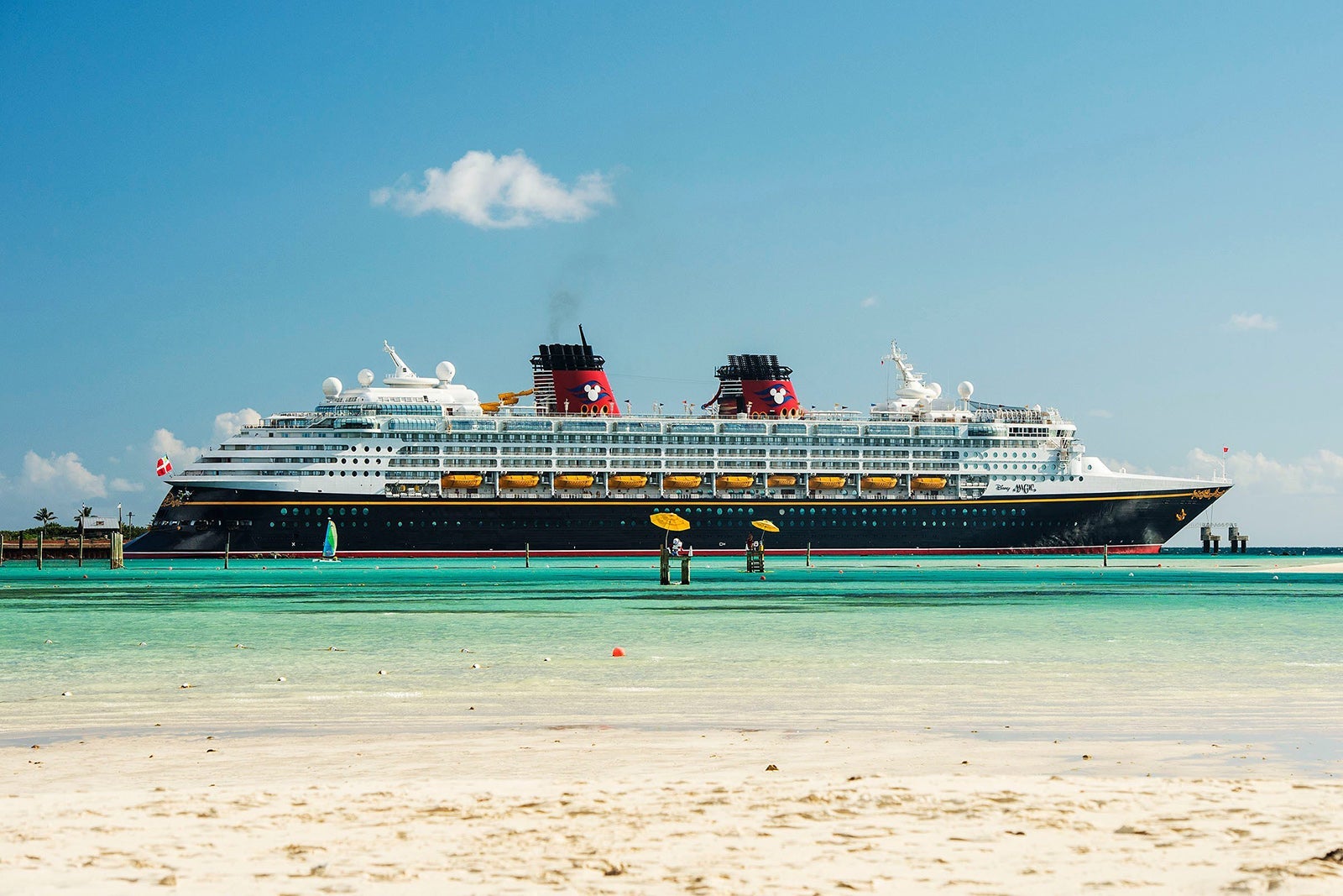 Disney Cruise Line ship Disney Magic docked on green water with blue sky in the background and sand in the foreground