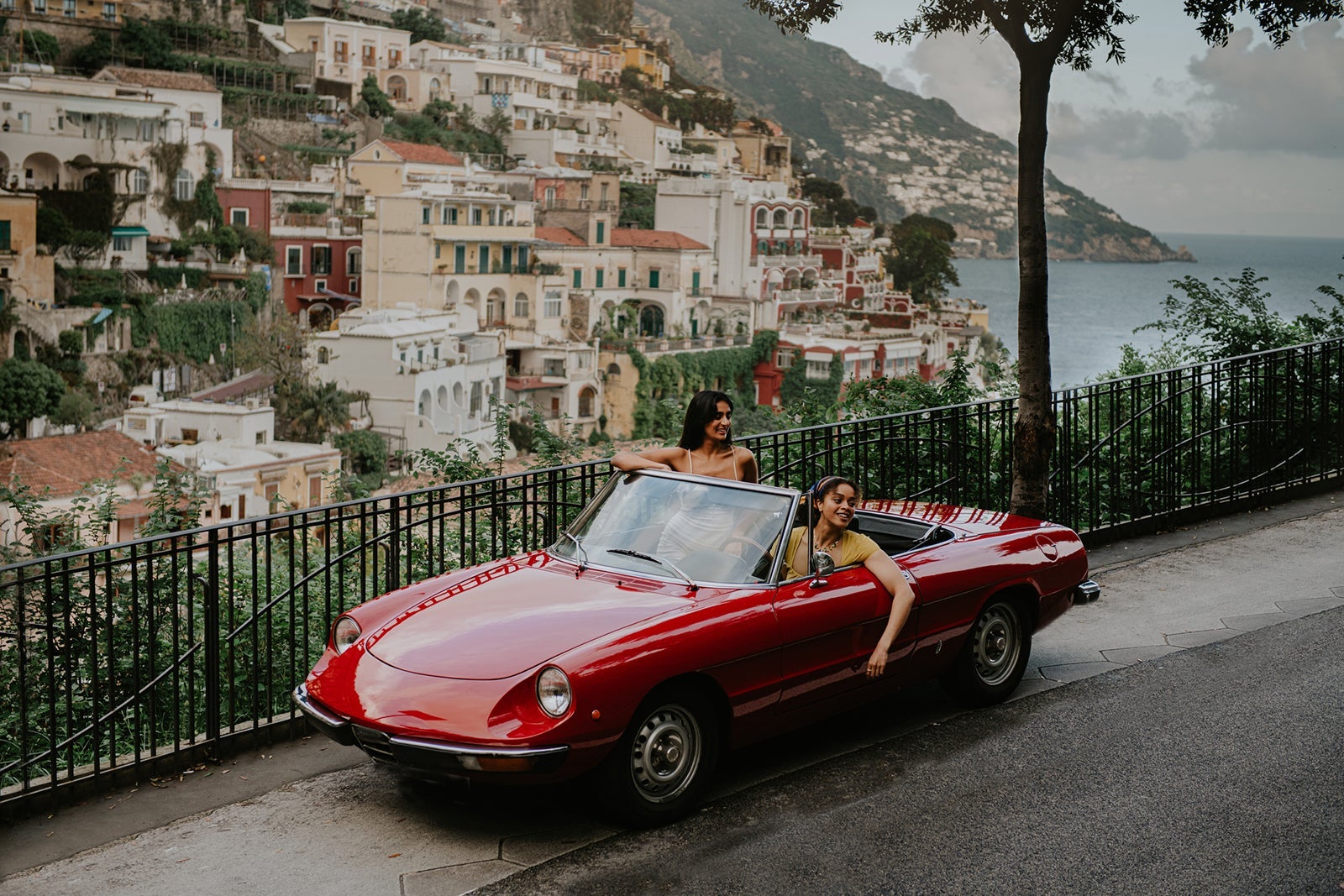 Wide shot of two woman in a vintage red convertible car in Positano, Italy.
