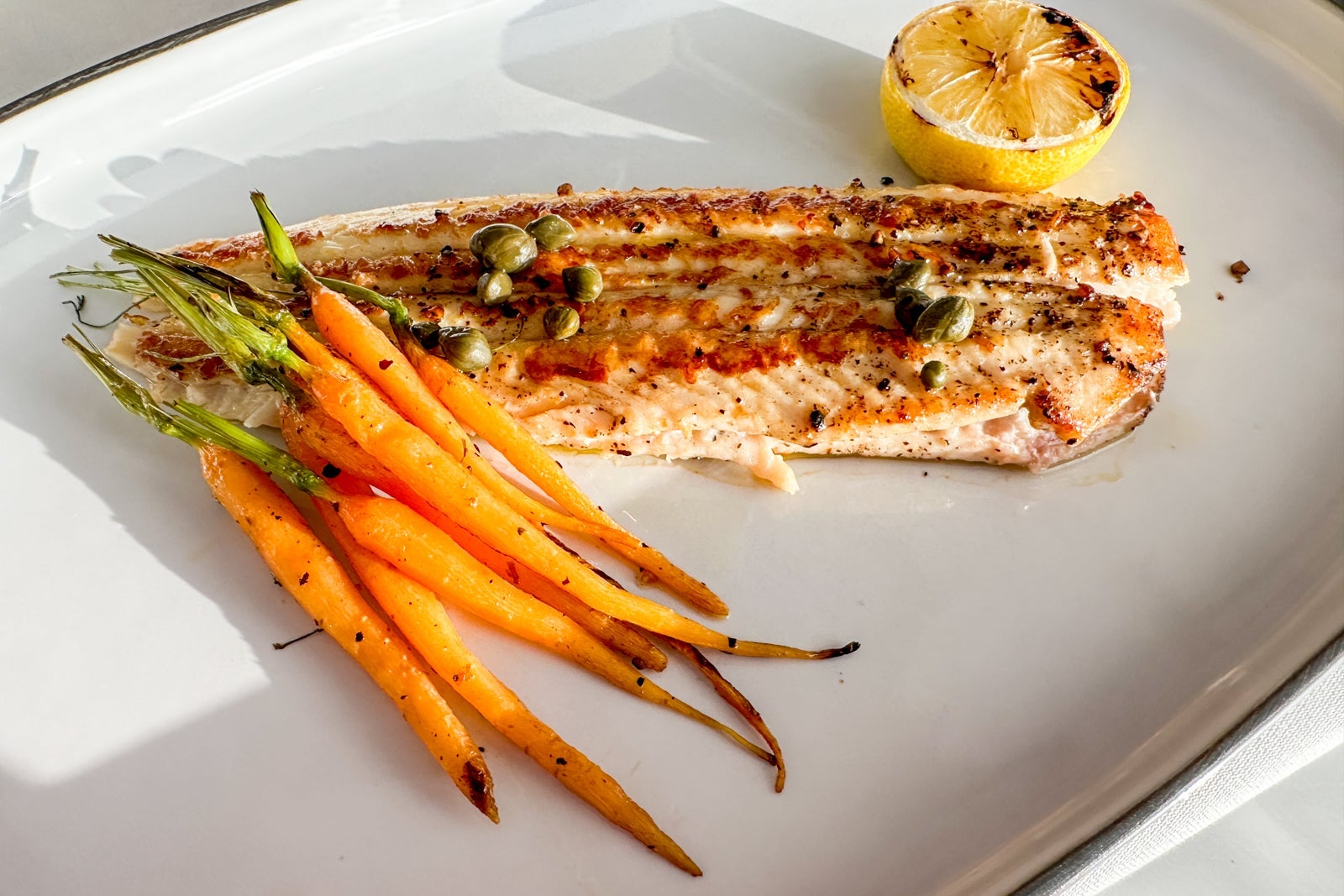 A white plate with thin whole carrots and a sole filet with lemon
