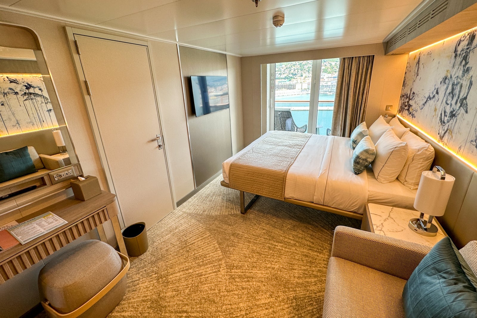 A cruise ship cabin with a balcony, connecting door, king-sized bed, couch, nightstands and vanity