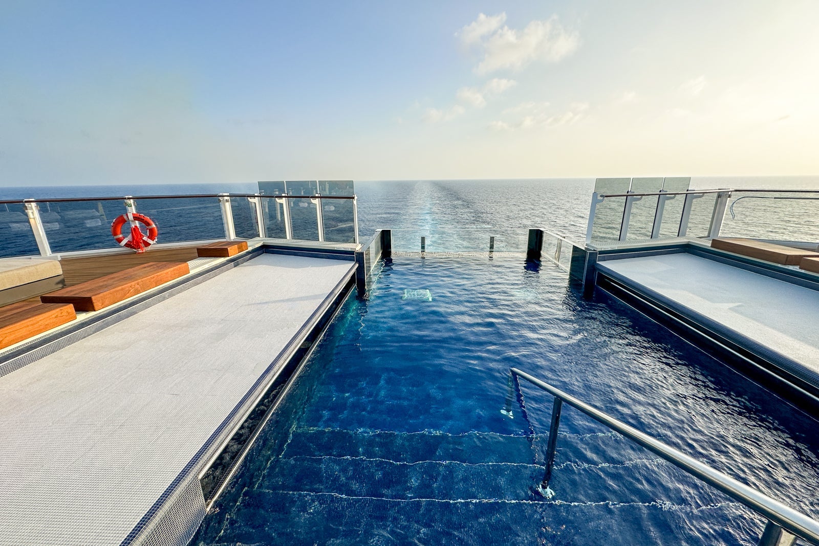 An aft-facing infinity pool on a cruise ship overlooking blue water and sky