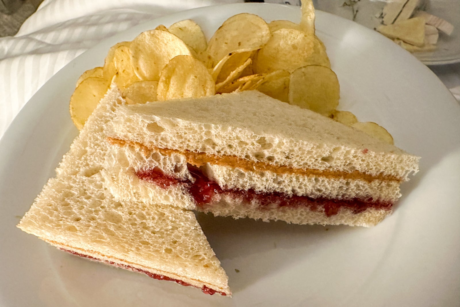 A peanut butter and jelly sandwich with potato chips on a white plate