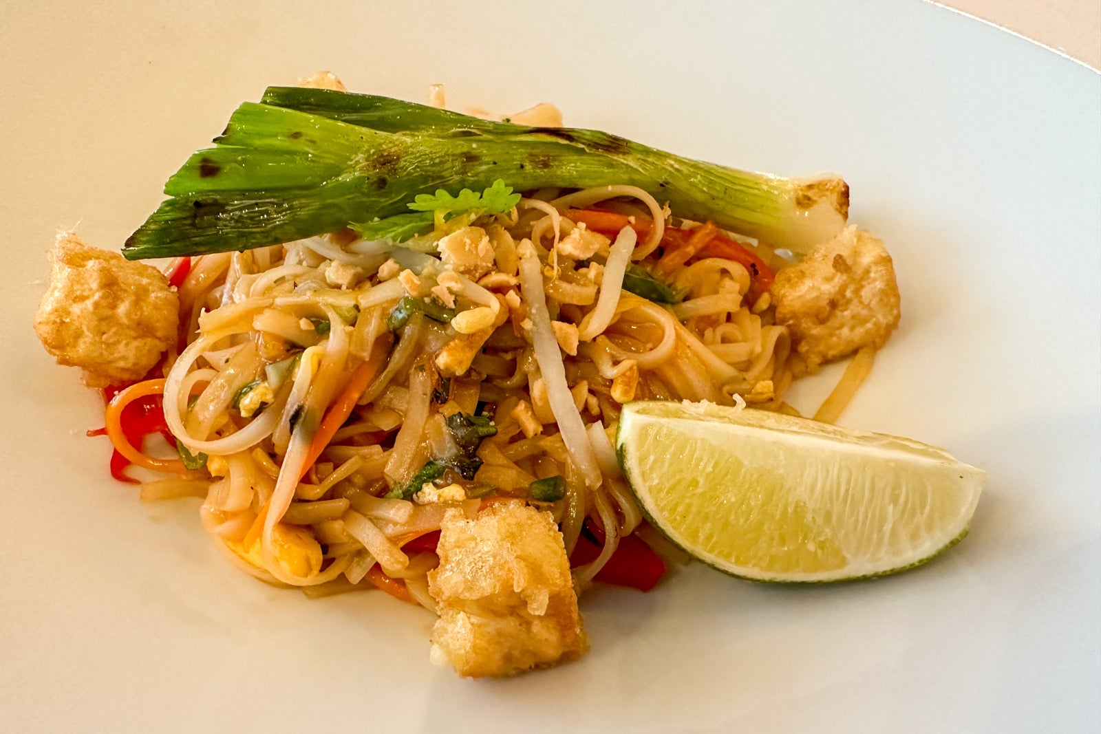 A plate of pad thai noodles with a lime