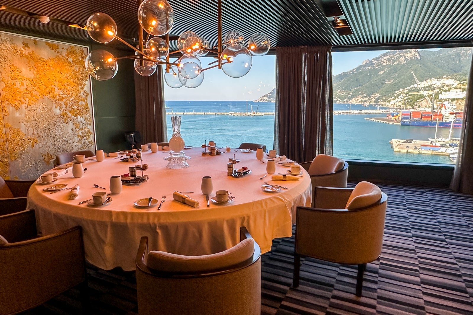 A fancy cruise ship dining room, featuring a bubble chandelier chairs and a round table set with a white tablecloth and dishes