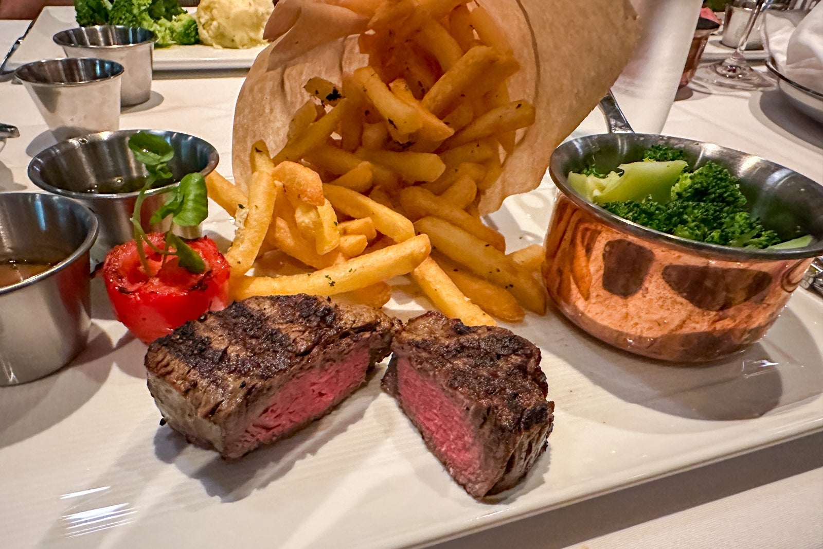 A white plate contains a small steak garnished with tomatoes, plus sides of vegetables and French fries