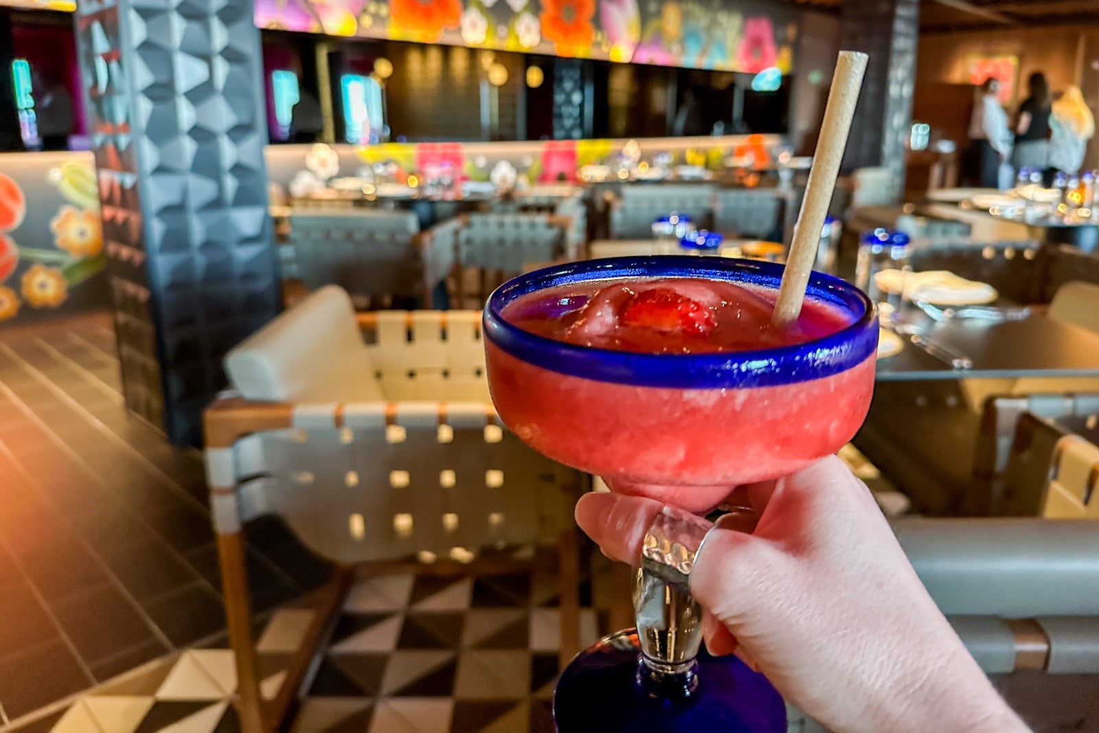 A hand holding a strawberry margarita with chairs in the background