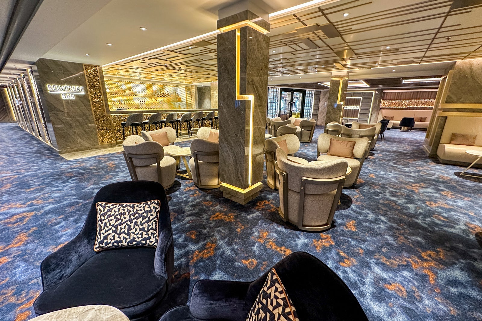 A gilded bar with blue carpeting and blue chairs on a cruise ship