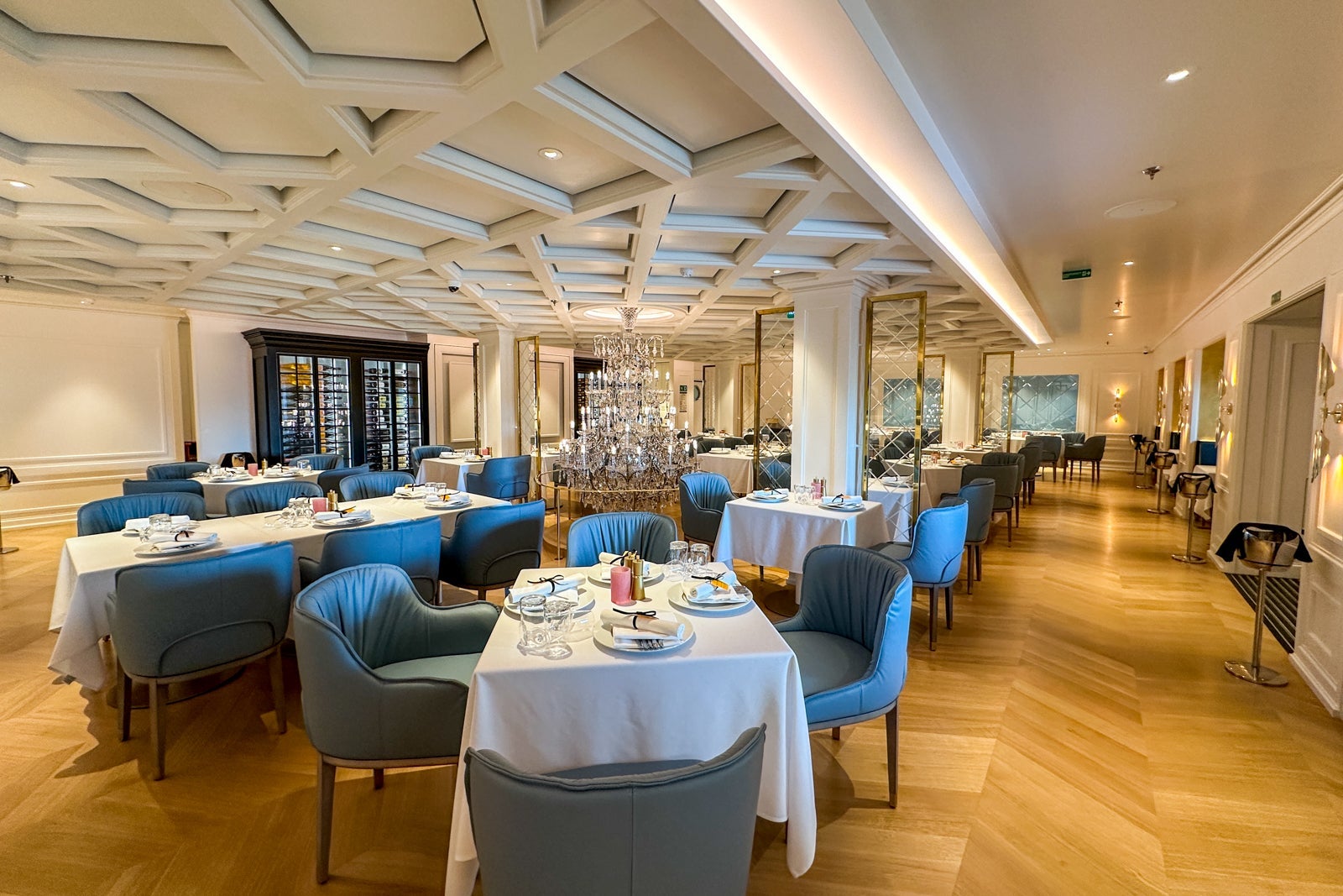A cruise ship restaurant with wooden flooring, blue chairs and tables with white tablecloths