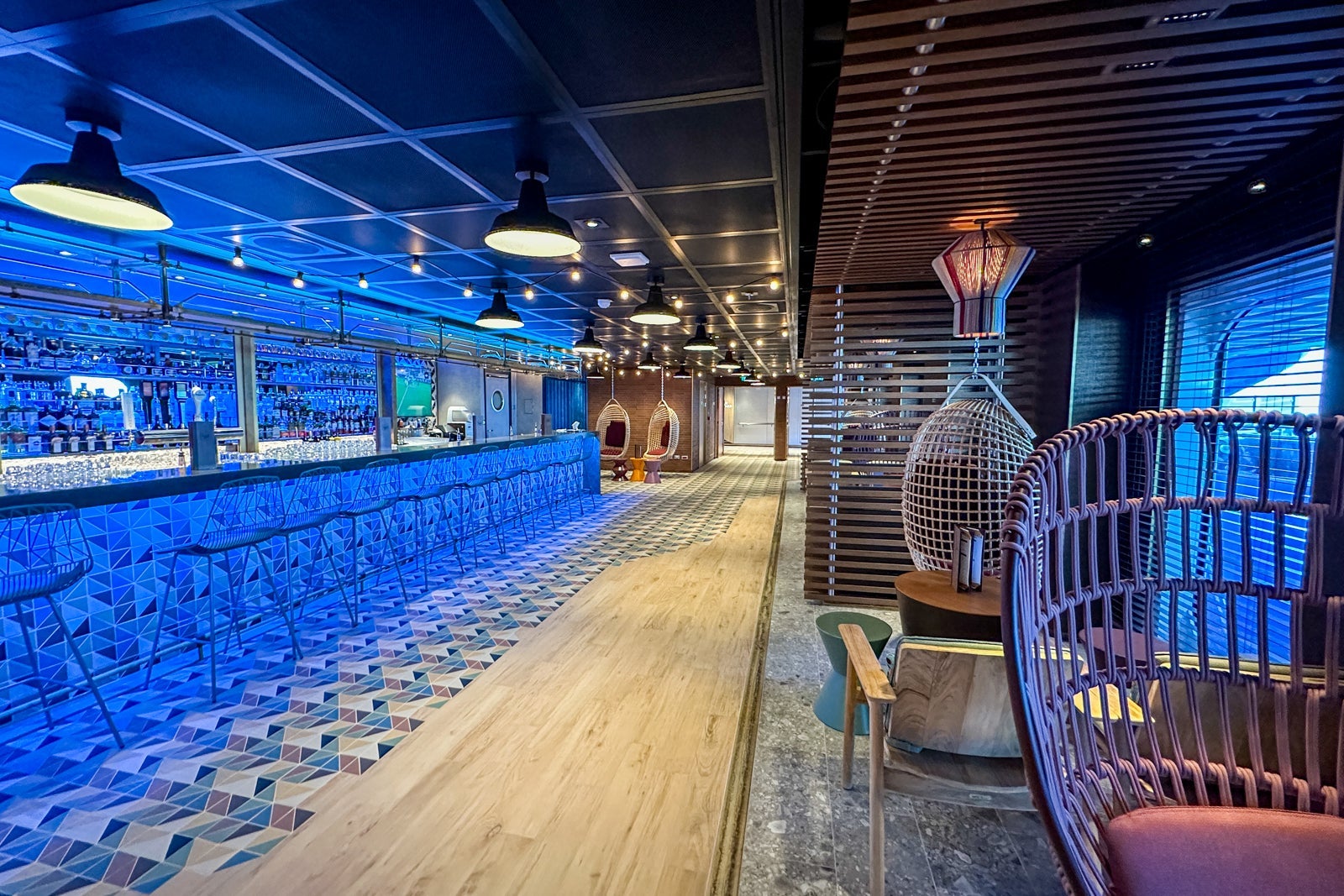 A walkway flanked on one side by a blue-lit bar and on the other by seating alcoves
