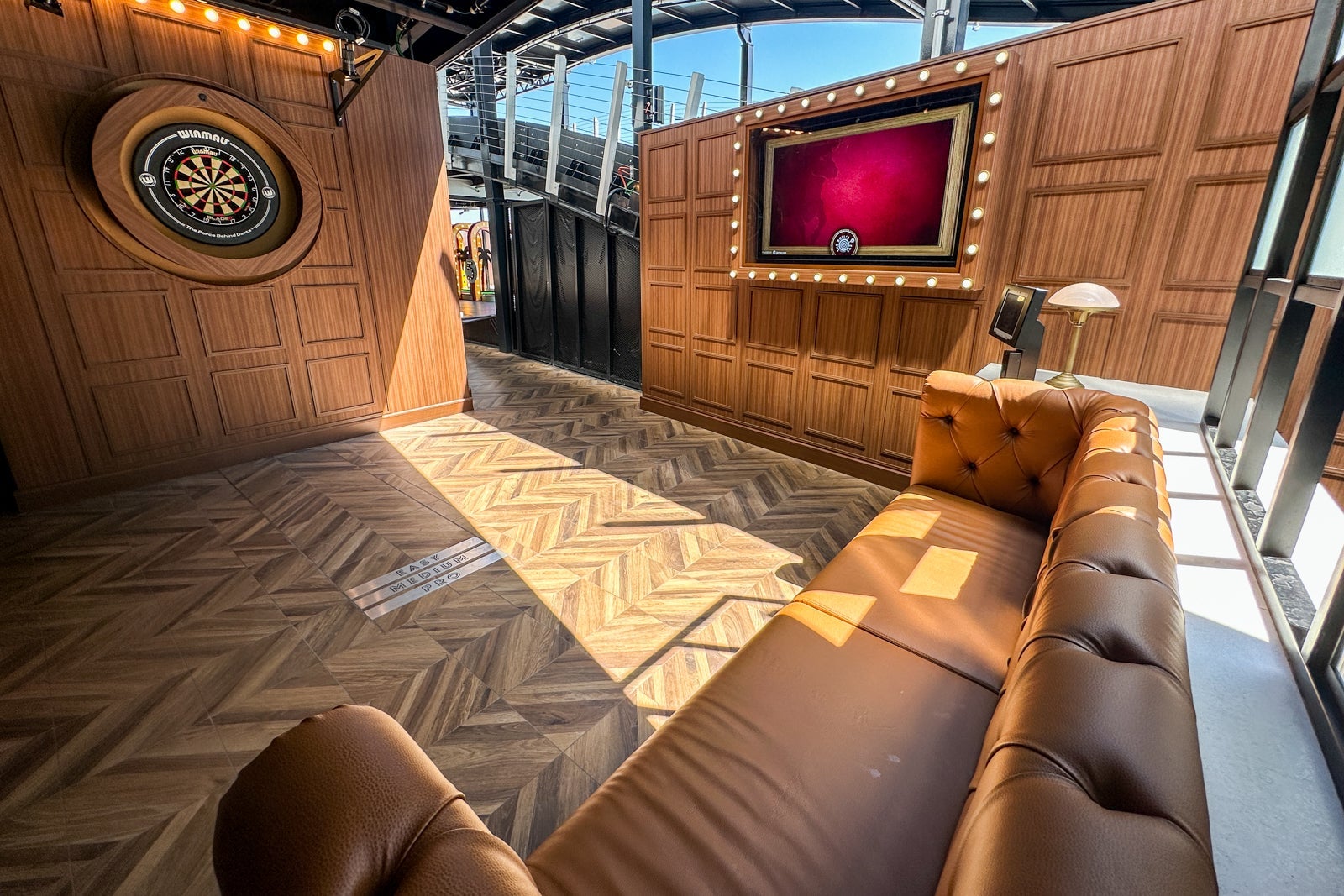 An alcove for darts with a dart board, sofa and wooden chevron floor on a cruise ship