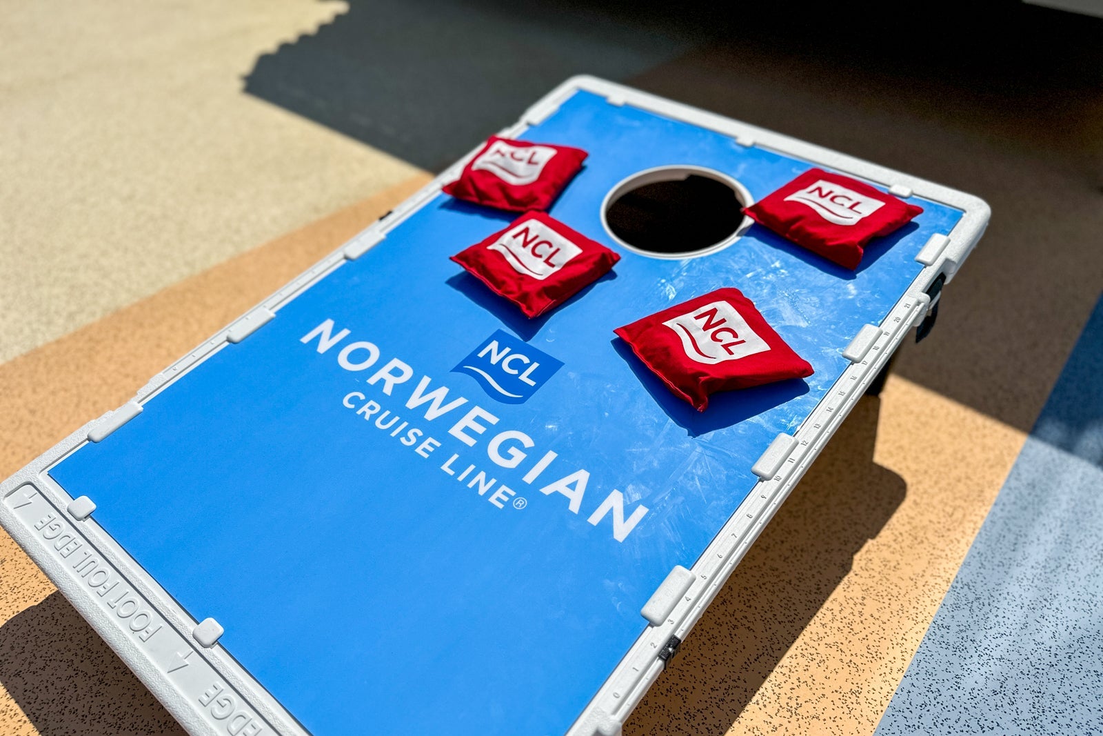 A blue cornhole board that says "Norwegian Cruise Line" and red beanbags that say "NCL"