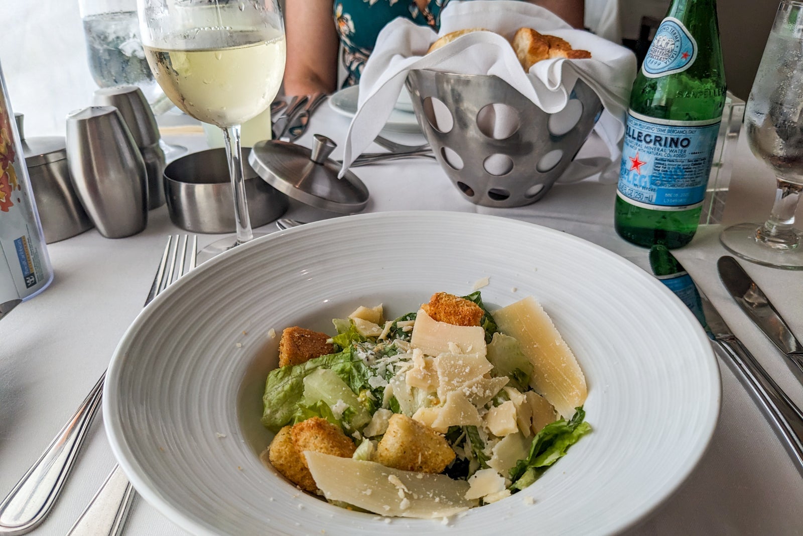 Caesar salad on a white bowl by a glass of white wine