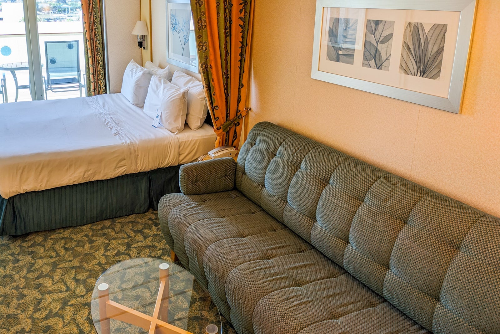 A cruise ship balcony cabin with a bed, couch and glass coffee table