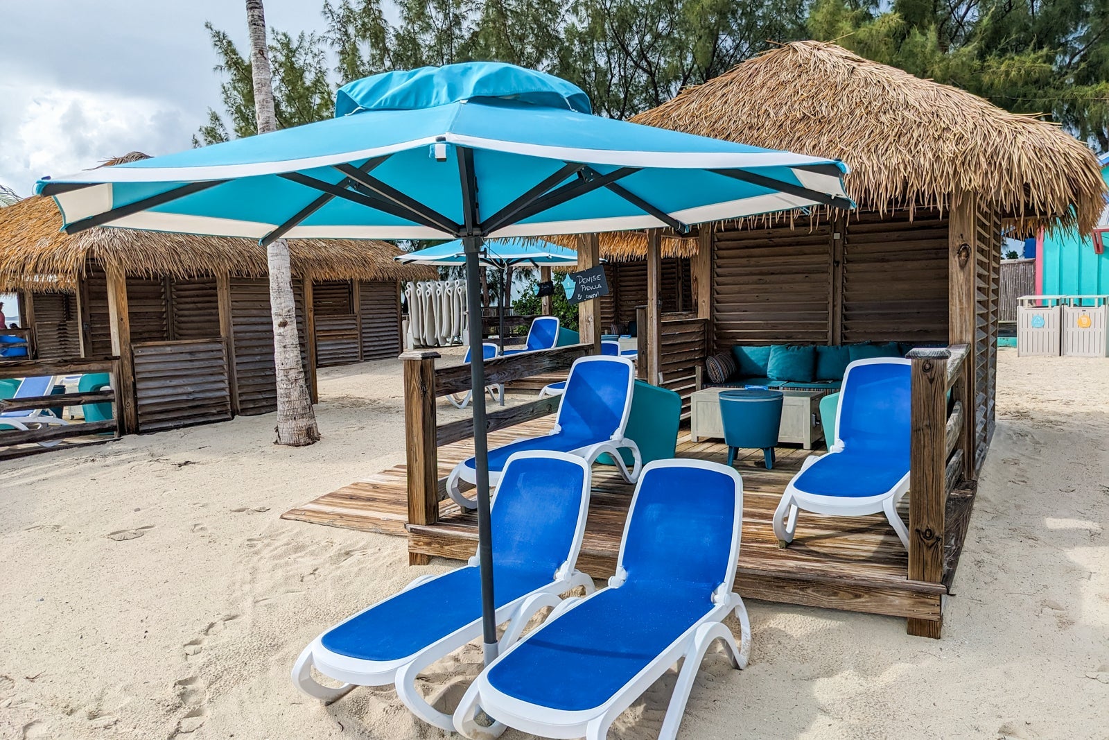 Thatched roof cabana with blue lounge chairs in front on the beach