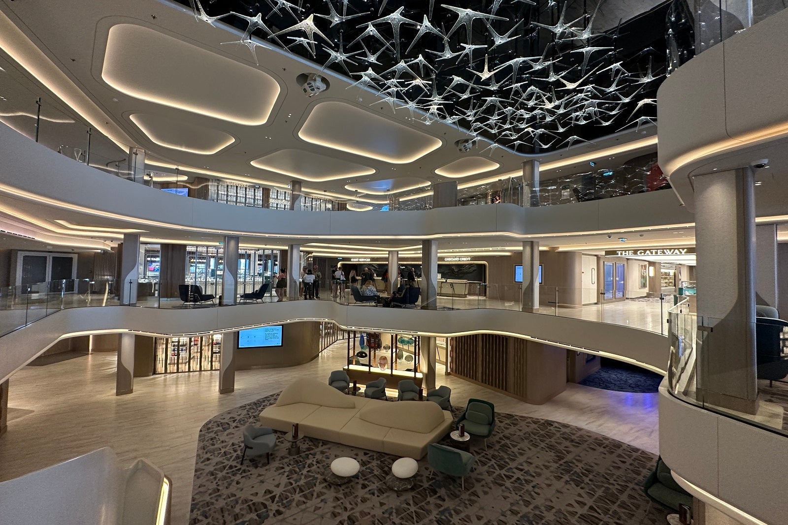 View of a three-deck cruise ship atrium from above with midcentury modern lighting overhead