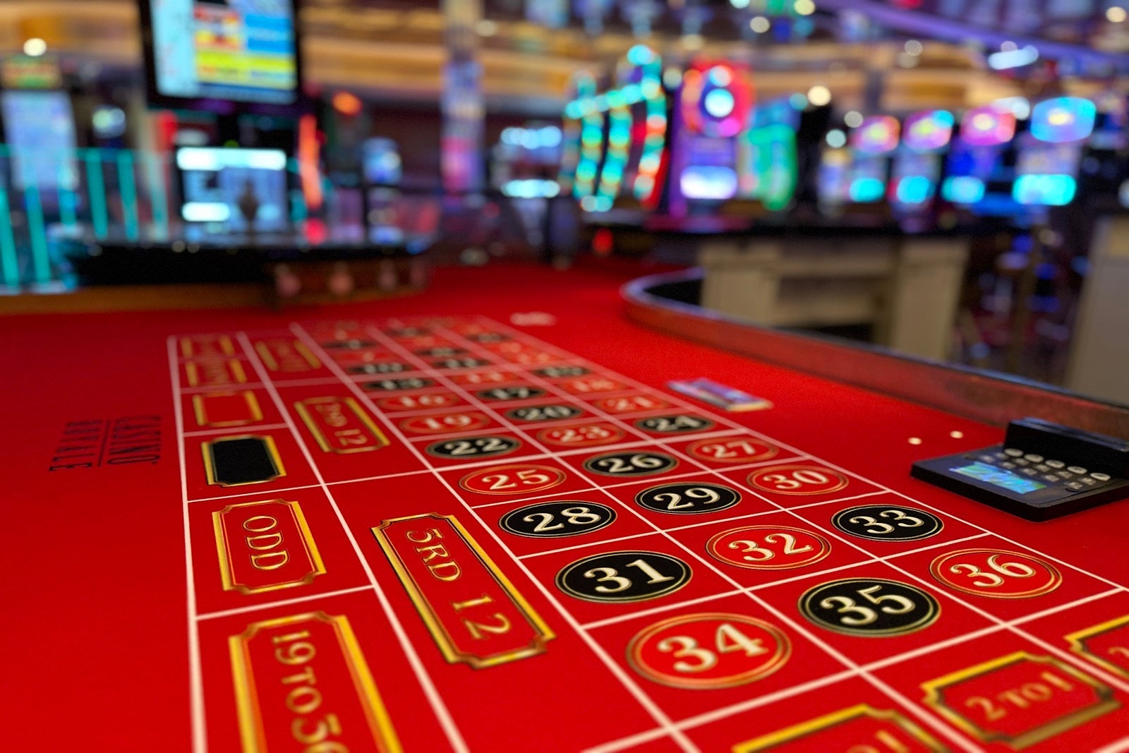 A close-up of a gaming table in a cruise ship casino with slot machines in the background