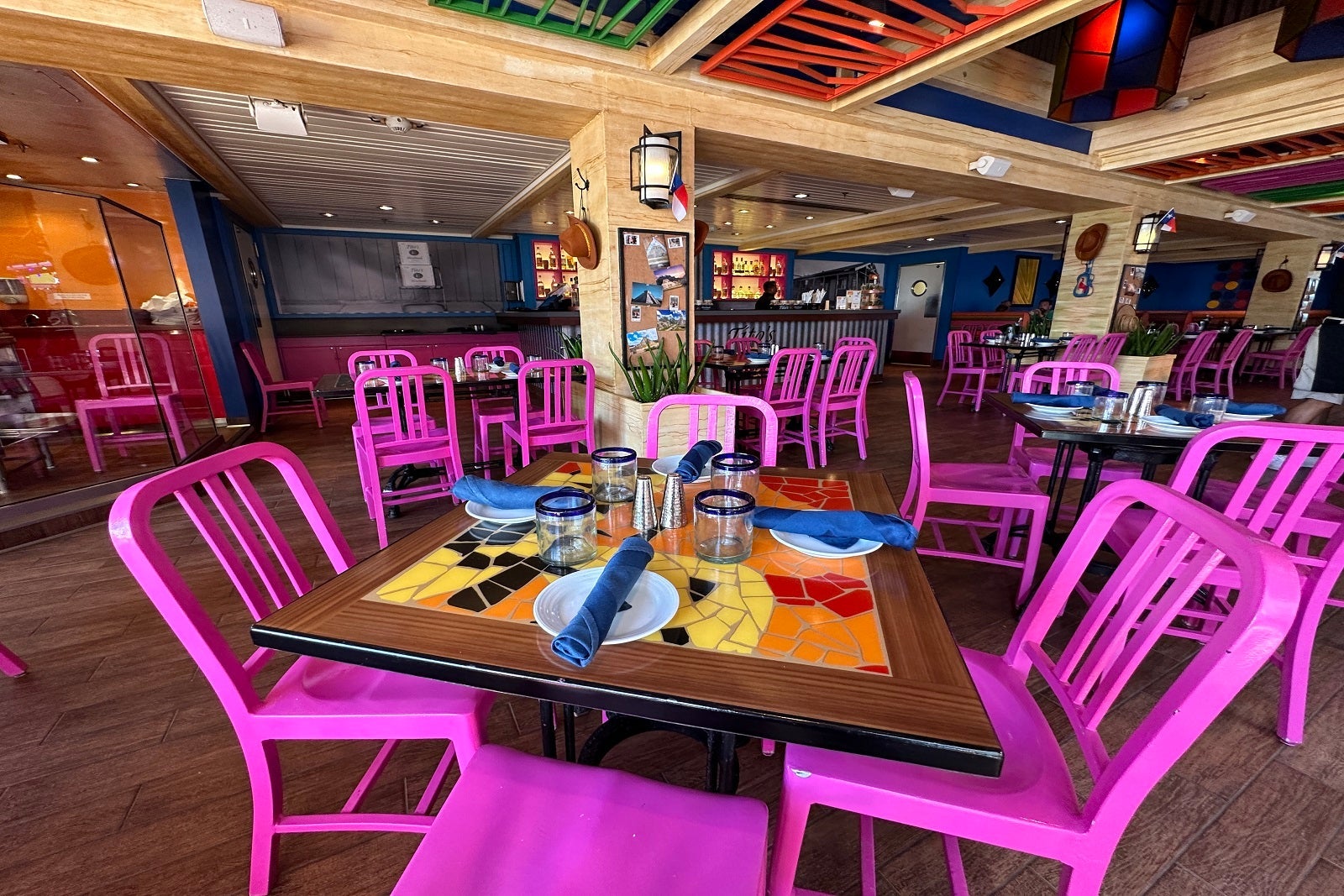 A wooden table topped with a colorful mosaic and surrounded by bright pink chairs